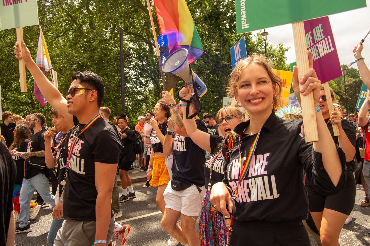 Stonewall pride march with people smiling and holding signs up advocating for LGBTQ+ rights